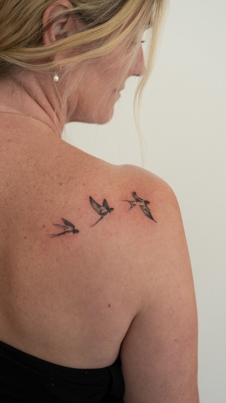 Fine line-tatuering med svalor på en kvinnas axel