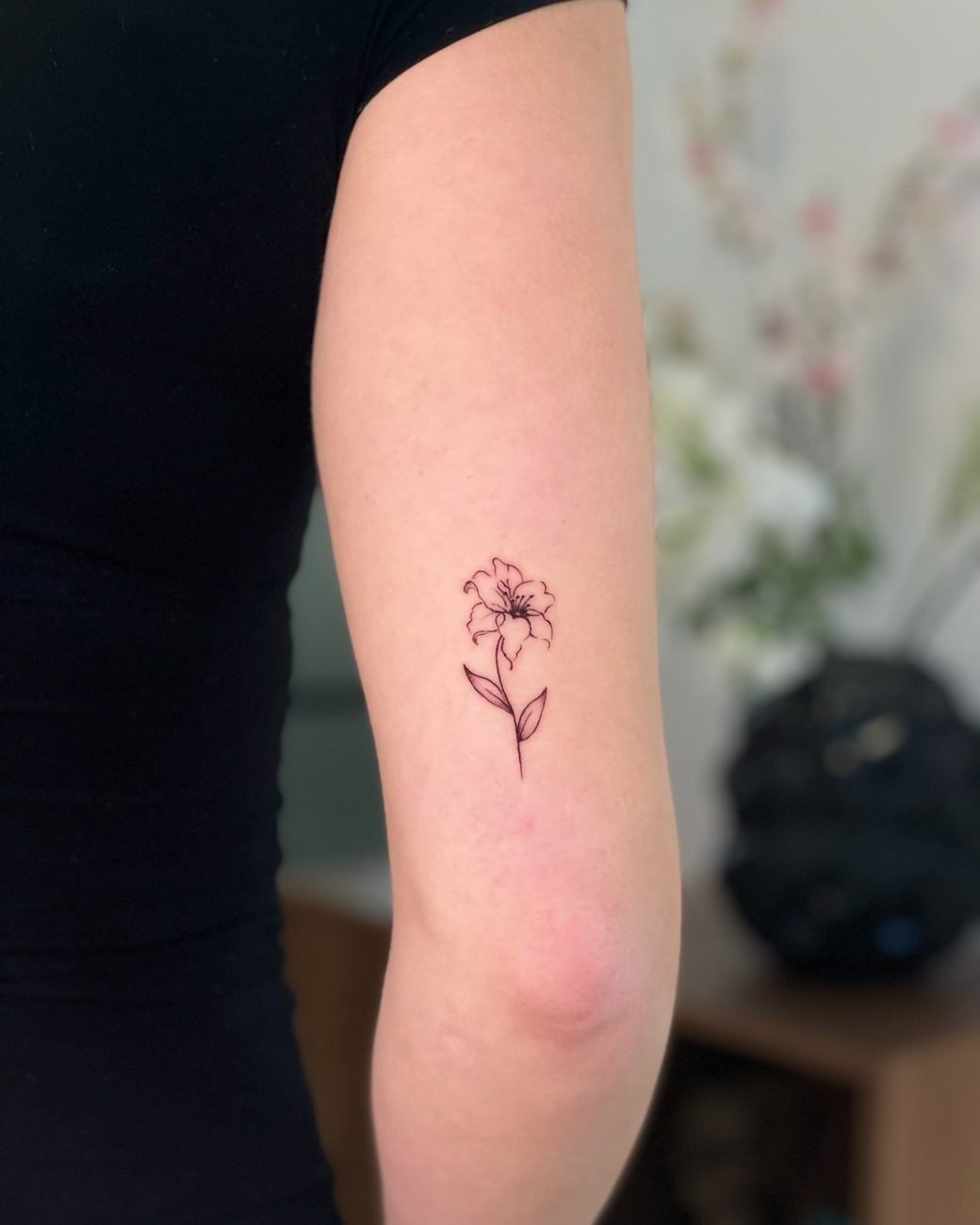 Fine line-tatuering av en lilja på överarmen