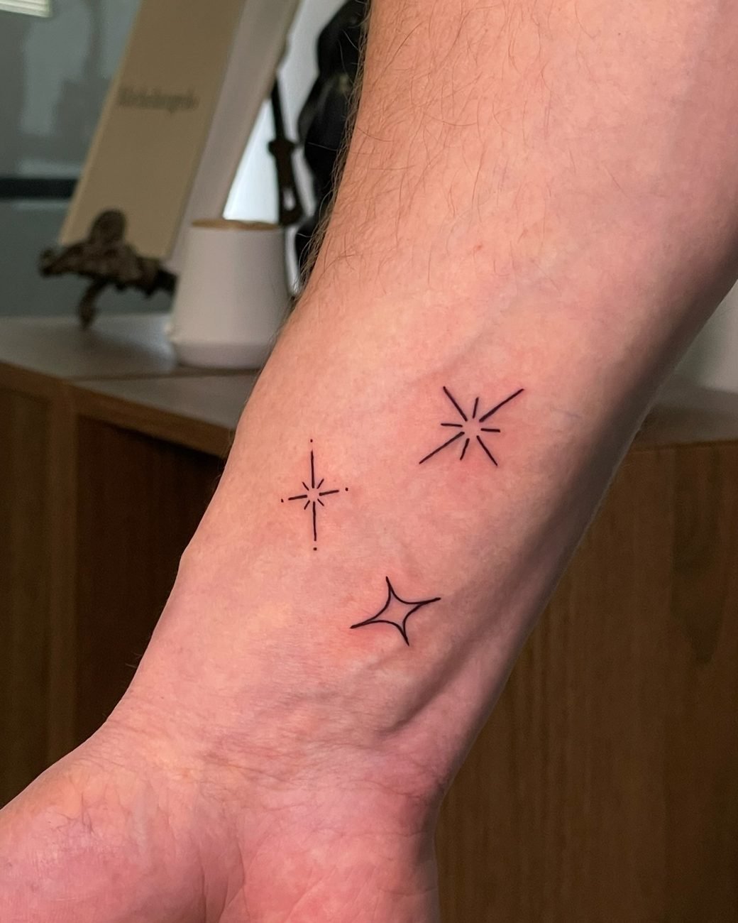 Fine line-tatueringar med gnistror och stjärnor på handleden